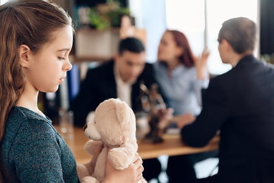 Young girl holding her stuffed animal while her parents argue